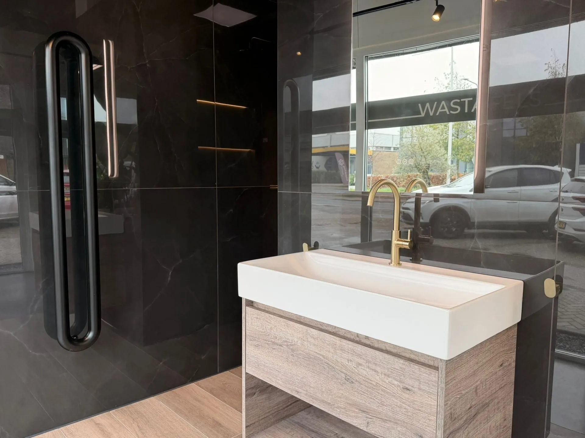 Wastafel met gouden kraan voor donkere tegels en een zwarte radiator
